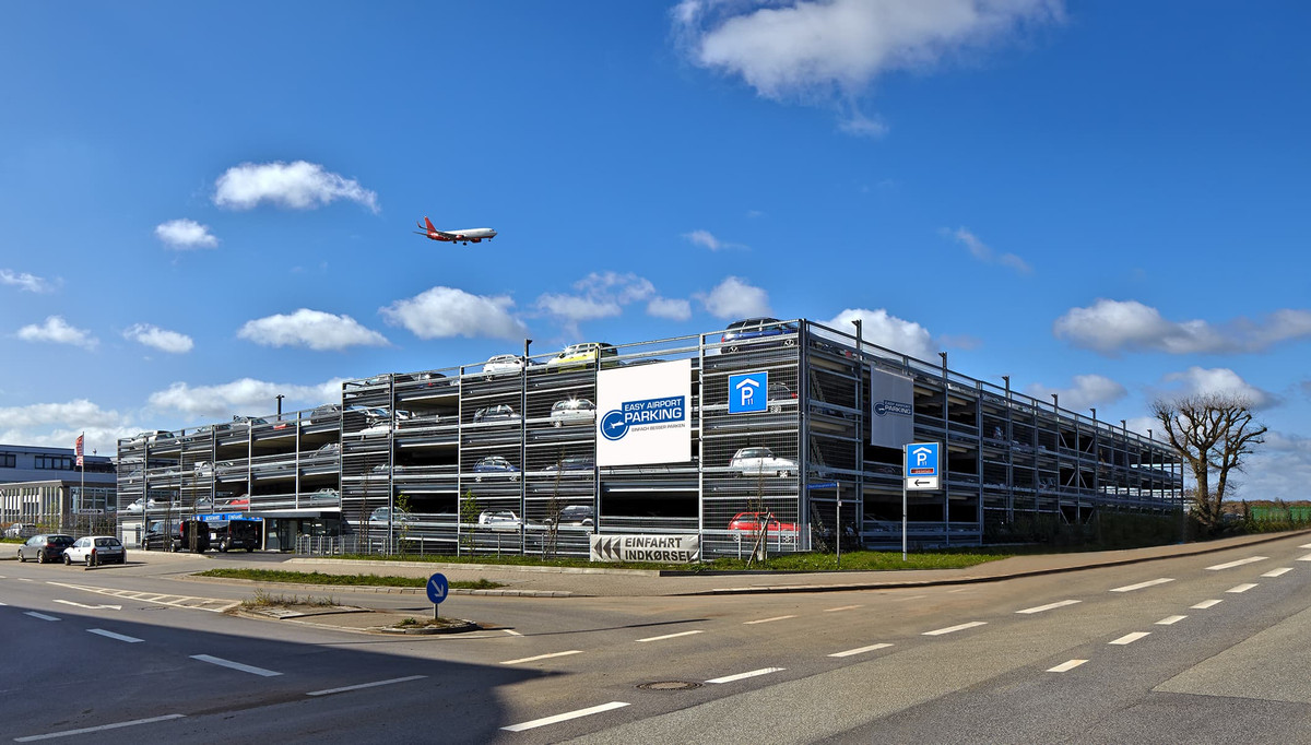 Straßenansicht des mehrstöckigen Easy Airport Parking Parkhauses mit landendem Flugzeug am Flughafen Hamburg (HAM)