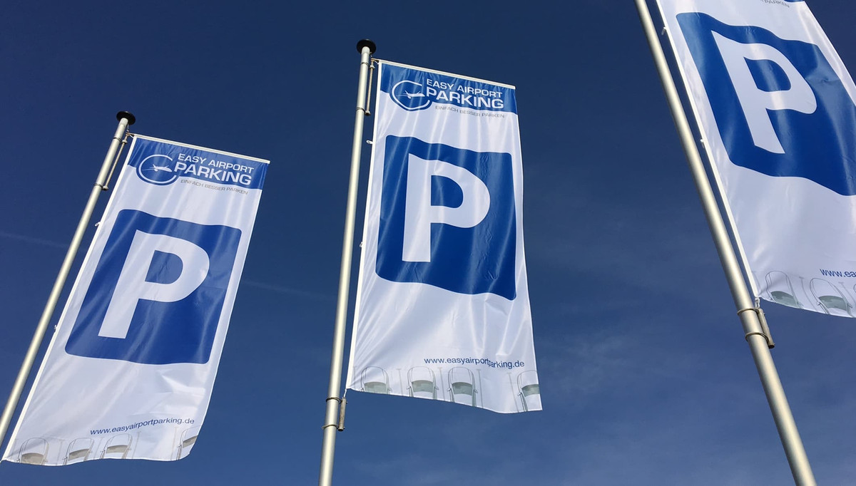 Tre flag med Easy Airport Parking-logo og parkeringssymbol på parkeringspladsen hos Easy Airport Parking i Frankfurt-Hahn Lufthavn (HHN)